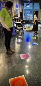 Three volunteers staffing the main lounge stand and sit among colorful, playful sensory items along the open floorspace.